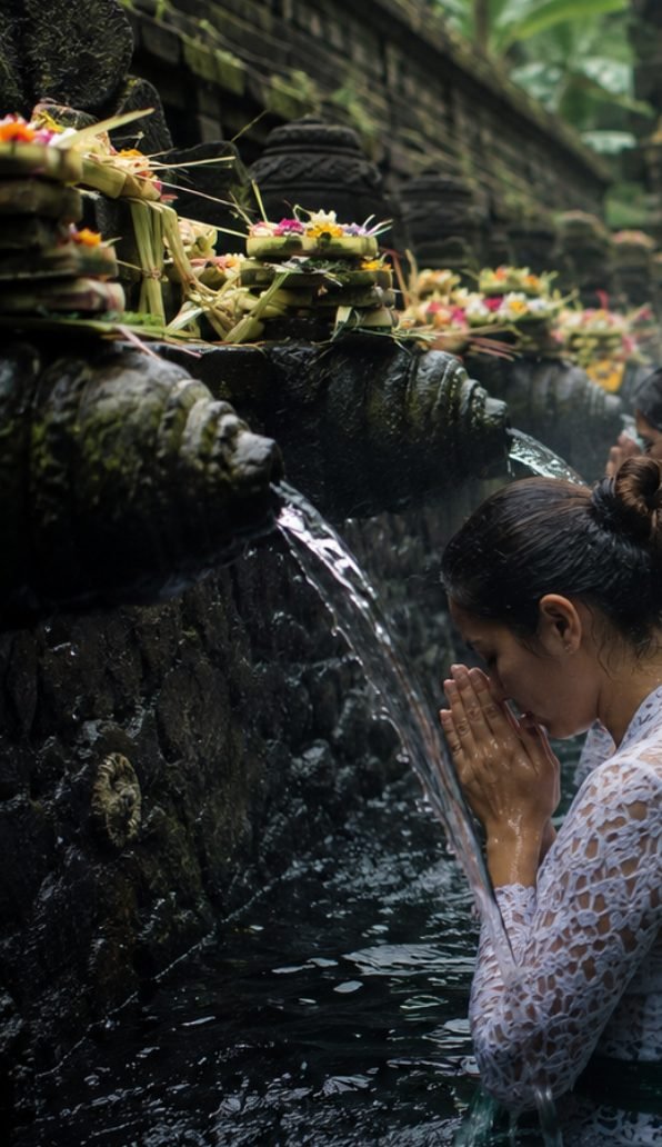 Mulher em oração diante das fontes de purificação de um templo balinês